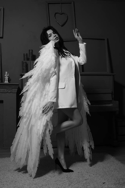 bela mulher morena em blazer e asas de anjo branco posando perto de piano no estúdio  - Foto, Imagem