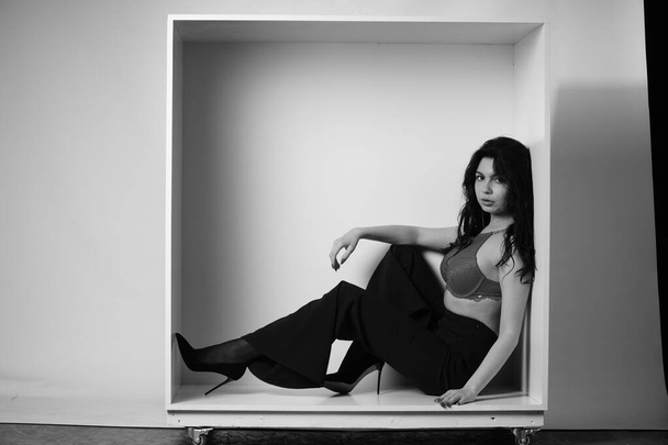 beautiful brunette woman wearing lingerie and pants posing in white cube at studio  - Foto, Bild