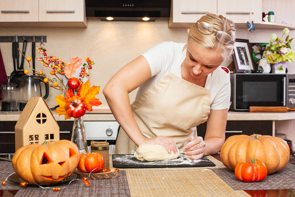Μια γυναίκα ζυμώνει ζύμη μπισκότων για το Halloween στην κουζίνα με φθινοπωρινή διακόσμηση. Άνετο σπίτι και προετοιμασία, Κάνοντας μπισκότα για το Halloween. - Φωτογραφία, εικόνα