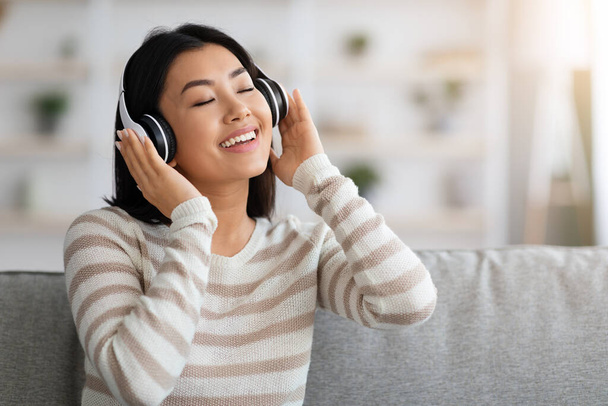 Portret van Relaxed Aziatische vrouw in hoofdtelefoon Luisteren muziek met gesloten ogen - Foto, afbeelding