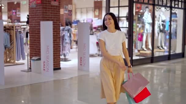 Mulher feliz deixando loja no shopping com muitos sacos de papel cheios de compras - Filmagem, Vídeo