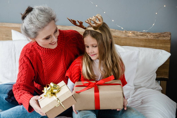 Családi karácsonyi koncepció. Vidám nagymama és az aranyos unokája ajándékot cserélnek. Család ajándékokkal a szobában. - Fotó, kép