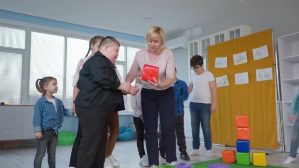 adaptación social para niños con discapacidades, alegres niños felices se divierten jugando con una maestra - Imágenes, Vídeo