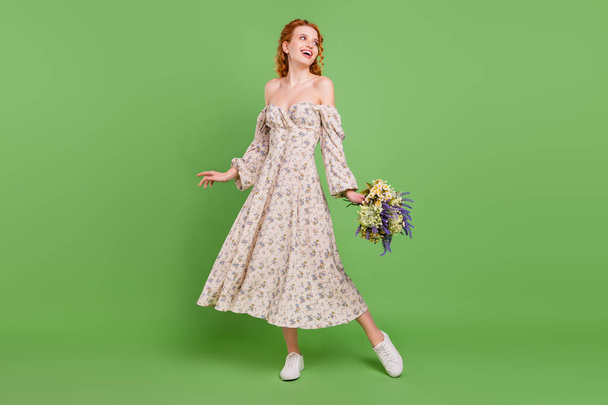 Full body photo of cute curly hairdo young lady hold bouquet look empty space wear dress isolated on pastel green color background - Foto, immagini