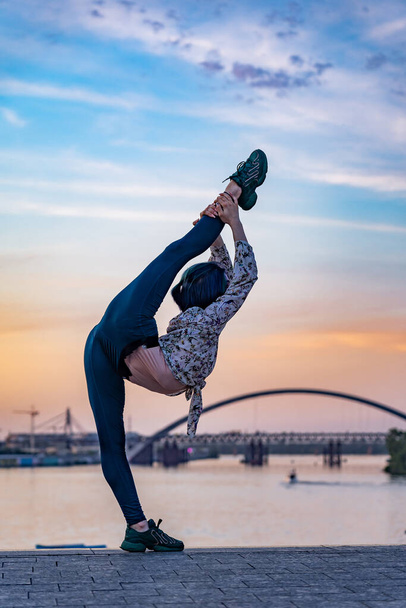 Silhouette of flexible female woman keeps balance gymnastic on split on the dramatic sunset. Concept of individuality, creativity and outstanding - Foto, Imagen