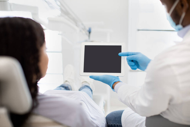 Dentiste noir montrant la tablette numérique avec l'écran blanc au patient féminin - Photo, image
