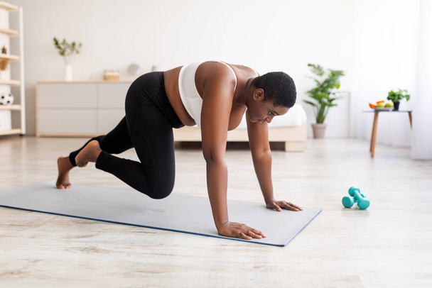 Ефективні вправи для тіла. Пишна чорна жінка робить тренування сили, біжить з руками на підлозі вдома
 - Фото, зображення