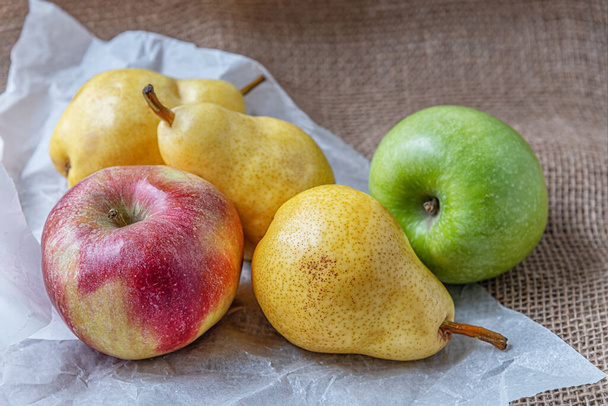 ripe juicy apples and pears on sackloth on white parchment - Фото, изображение