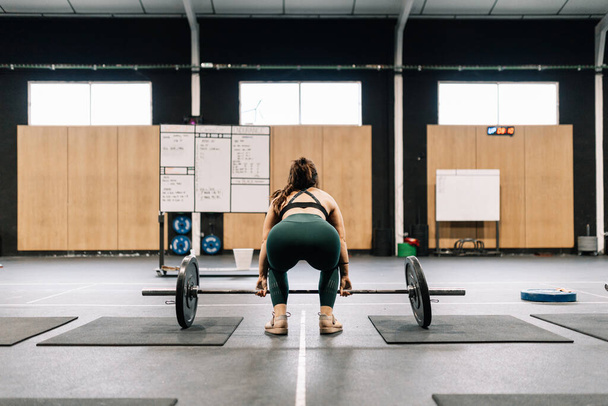 Joven mujer de fitness haciendo sentadillas de barra en un gimnasio - Foto, imagen