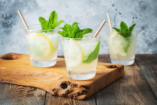Два бокала с лимонадом или мохито с лимоном и мятой, прохладительный напиток или напиток со льдом на деревенском синем фоне - Фото, изображение