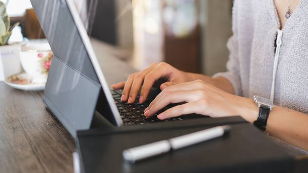 Serbest çalışan genç bir kadının tahta masada dizüstü bilgisayarın tuşlarına yazı yazması.. - Fotoğraf, Görsel