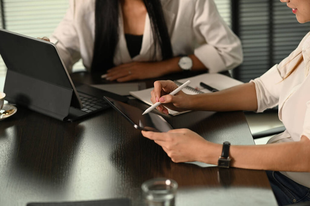 Prise de vue recadrée de deux femmes d'affaires utilisent une tablette numérique pour discuter de l'information dans la salle de réunion. - Photo, image