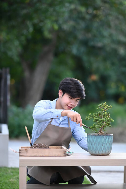 Egy fiatal férfi portréja, aki bonsai fát ültet otthon a fazékba.. - Fotó, kép