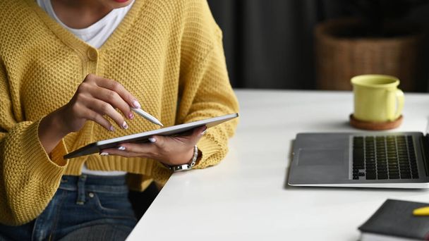 Обрезанный снимок молодой женщины с помощью цифрового планшета и перо стилуса во время работы на ноутбуке в офисе. - Фото, изображение