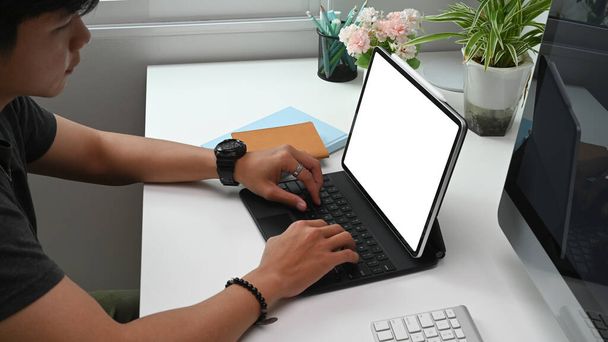 Crop shot του νεαρού άνδρα freelancer χέρια δακτυλογράφηση στο πληκτρολόγιο tablet στο δημιουργικό χώρο εργασίας. - Φωτογραφία, εικόνα