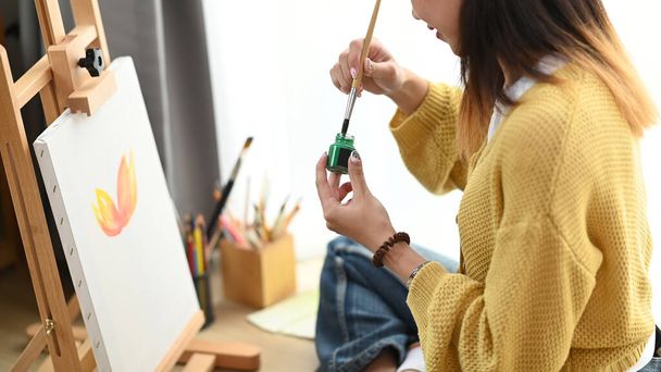Resim stüdyosunda elinde fırça tutan ve renkli şişeye bandıran kadın ressamın kırpılmış görüntüsü.. - Fotoğraf, Görsel