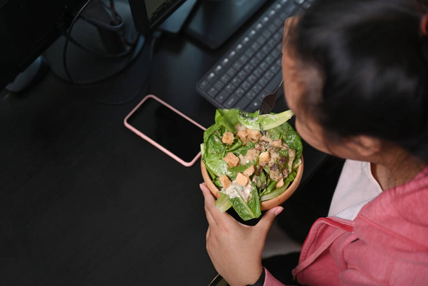 Yli pään laukaus nainen ylipainoinen ottaa tuoretta salaattia lounaalla työpaikallaan. - Valokuva, kuva