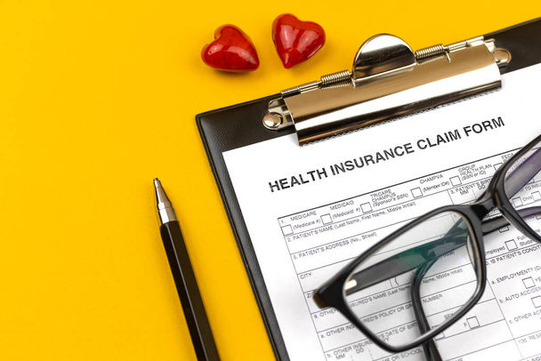 Formulaire de demande d'assurance maladie. Bureau d'affaires avec presse-papiers, stylo et cœurs rouges sur un bureau jaune. Vue du dessus  - Photo, image
