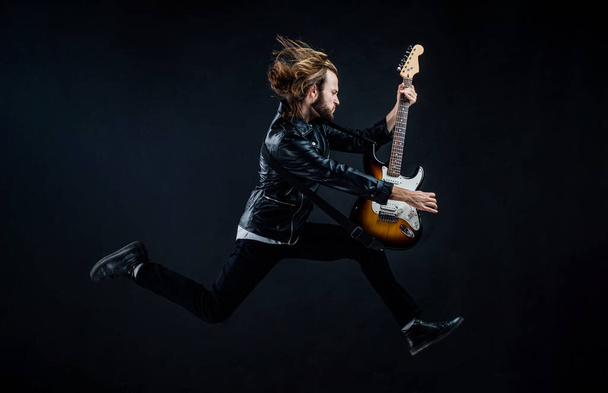 emotional bearded rocker in leather jacket. man long hair play electric guitar. - Foto, afbeelding