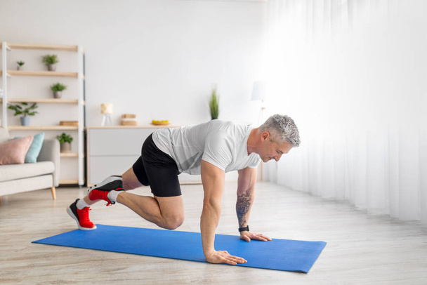 Homme mûr sportif faisant des exercices de course sur planche sur tapis de sport dans le salon à la maison, espace libre - Photo, image