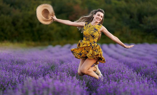 Beautiful young woman at sunset jumping for joy in a lavender field in full bloom - Foto, imagen