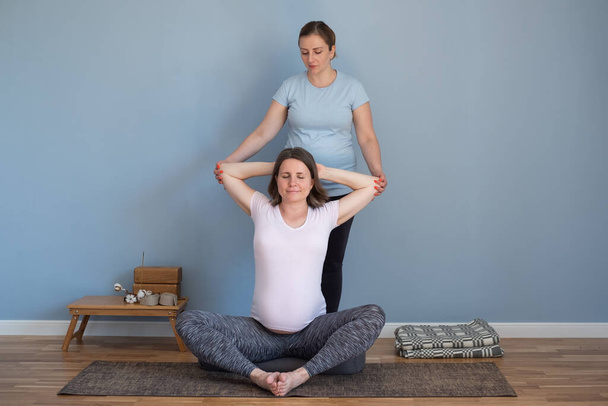 Antrenör, hamile bir kadının omuzları için yoga yapmasına yardım ediyor. - Fotoğraf, Görsel