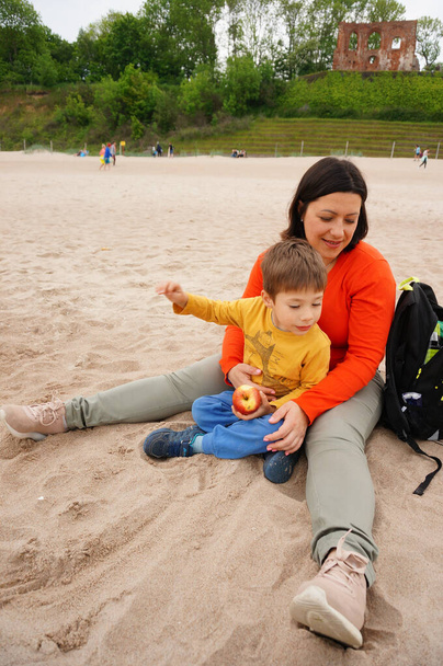 TRZESACZ, POLAND - Jun 04, 2021: A woman sitting with her son on the sand at a beach in Trzesacz - Fotoğraf, Görsel