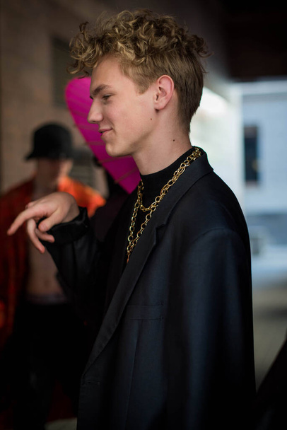 Adolescente masculino positivo com cabelo encaracolado vestido com roupas de rua com correntes ao redor do pescoço para uma caminhada. Juventude e estilo de vida conceito. - Foto, Imagem