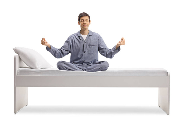 Man wearing pajamas and practicing yoga on a bed isolated on white background - Φωτογραφία, εικόνα