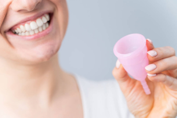 Close-up portrait of smiling Caucasian woman holding pink menstrual cup on white background. Alternative to tampons and pads on critical days. - Фото, изображение