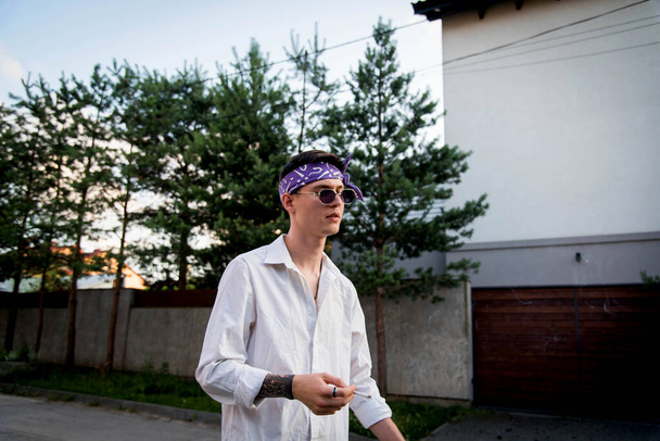 Pozitív férfi kendővel öltözött utcai ruhák láncok körül nyak és lila kendőt sétálni. Fiatalság és életmód koncepció. Rap művész új iskola. Dohányzás. - Fotó, kép