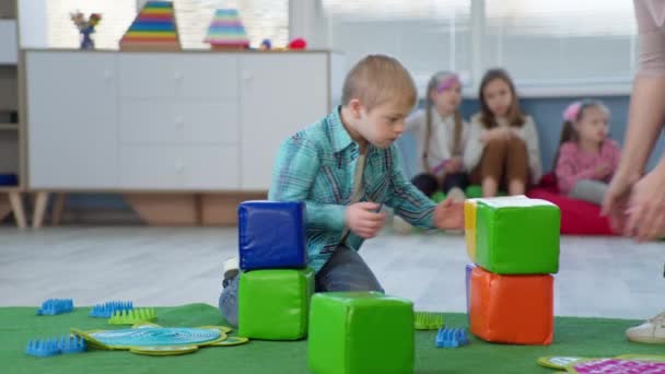 Porträts von kleinen Jungen mit Down-Syndrom-Bauturm aus farbigen Ziegeln während pädagogischer Aktivitäten für Kinder - Filmmaterial, Video