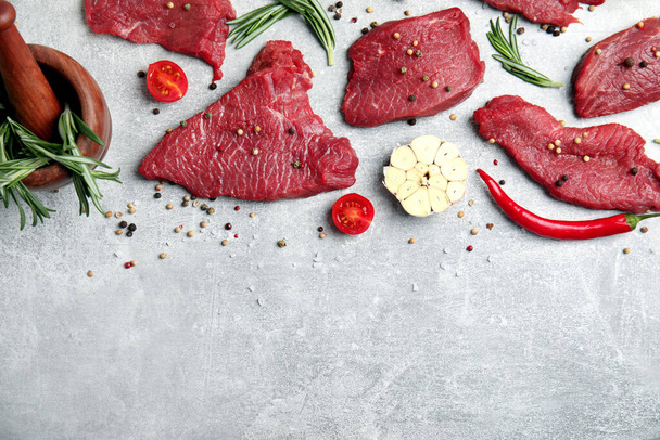 Fresh raw meat steaks and spices on light grey table, flat lay. Space for text - Фото, изображение
