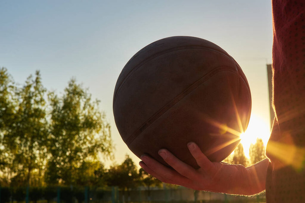 Gros plan d'un joueur de basket professionnel tenant une balle dans la main. Athlète de basket de rue avec une balle et un ciel bleu en arrière-plan - Photo, image
