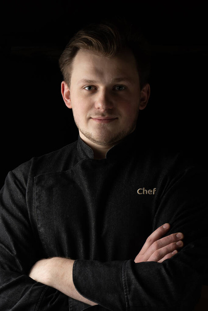 Porträt eines jungen Kochs in einer Jacke auf dunklem Hintergrund - Foto, Bild