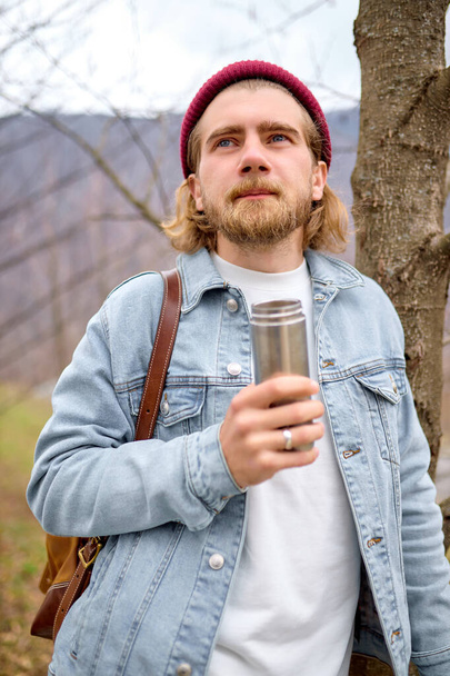 young handsome brutal bearded man traveling in the wild nature with thermos - Fotoğraf, Görsel