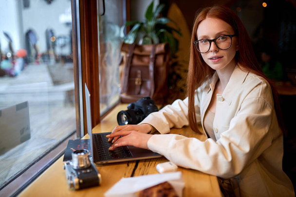 カフェでラップトップコンピュータを使用している自信のある女性旅行者、コーヒーショップで働く. - 写真・画像