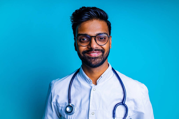 young latin hispanic medican man wear eye glasses with stethoscope in blue studio wall background - Foto, Imagen