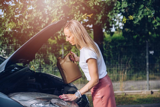 The blonde woman refills the oil in her car. - Photo, image