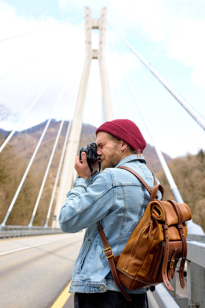 Handsome hipster young guy walking on bridge in urban area taking photo on camera - Фото, изображение