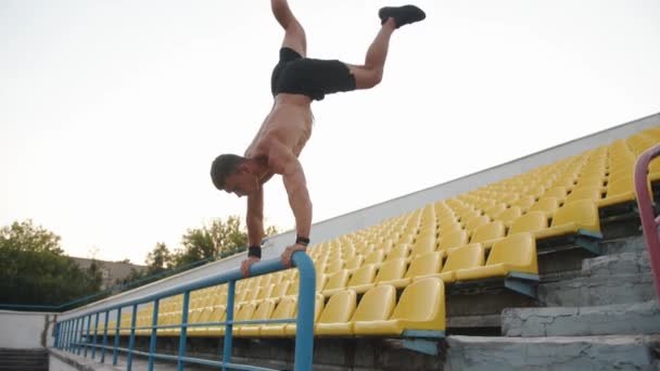 М'язистий чоловік займається спортом на стадіоні і робить тумбочку, спираючись на перила трибуни. Повільний рух
 - Кадри, відео