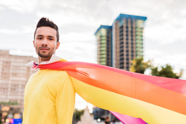 Νεαρός Λατίνος ομοφυλόφιλος με σημαία ουράνιο τόξο παρέλαση γκέι. Κάπα υπερήρωα τρόπου ζωής  - Φωτογραφία, εικόνα