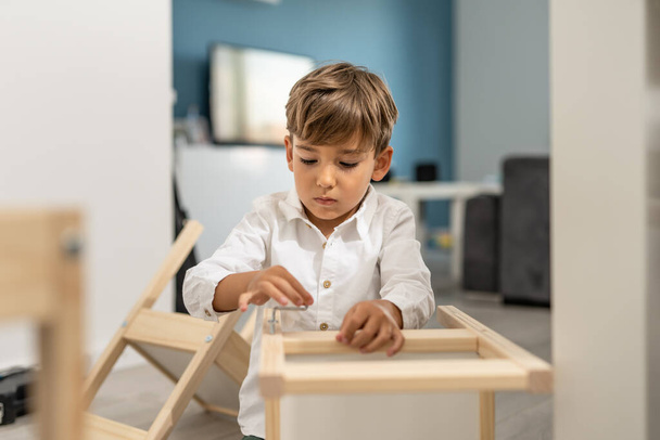 Kafkasyalı küçük bir çocuk, dört yaşında, kendini montajlayan bir sandalyeyle ya da evde masada oynuyor. Küçük bir çocuk, tek başına mobilya montajı yapıyor. - Fotoğraf, Görsel