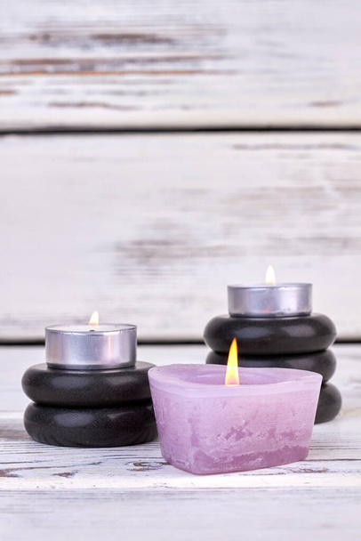 Vertical shot burning candles with black polished stones for spa. - Foto, imagen