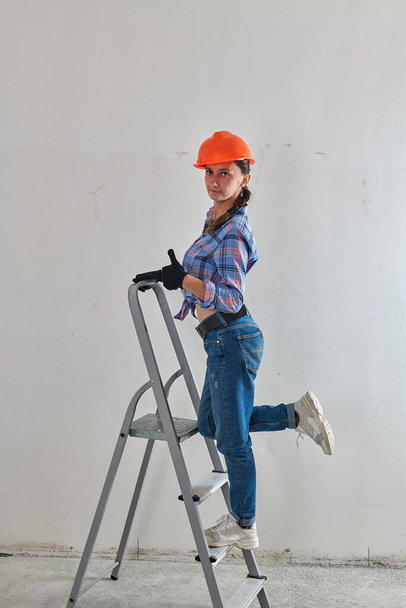 girl in an orange helmet and jeans on a stepladder - Zdjęcie, obraz
