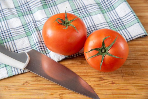 Два свіжих стиглих помідори на кухонному рушнику з ножем на дерев'яній обробній дошці
 - Фото, зображення