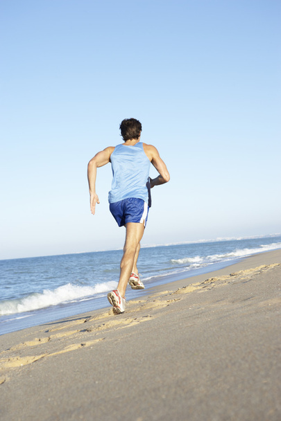 Young Man In Fitness Clothing Running Along Beach - Foto, afbeelding