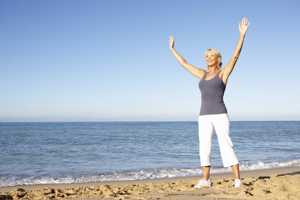 Senior Woman In Fitness Clothing Stretching On Beach - Zdjęcie, obraz