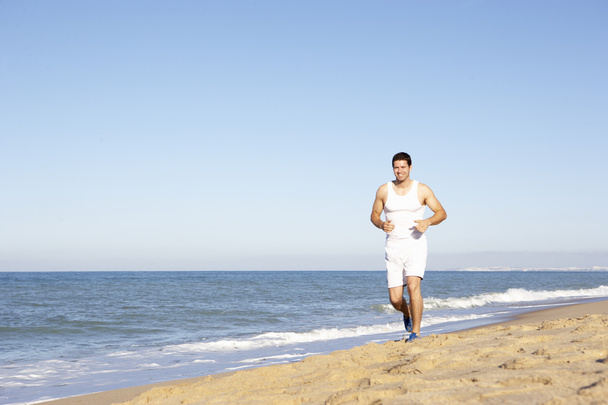 fiatal férfi fitness ruházat strand mentén futó - Fotó, kép
