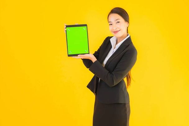 Portret mooie jonge aziatische vrouw gelukkig glimlach met slimme tabletten apparaat op geel geïsoleerde achtergrond - Foto, afbeelding